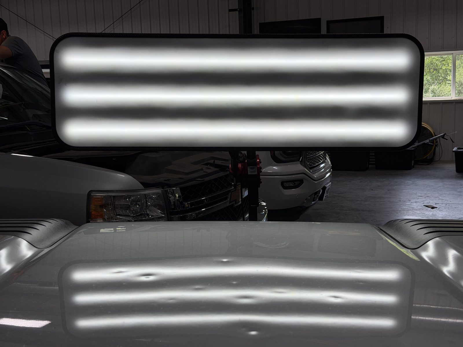 Hail dents on a vehicle hood shown under a PDR reading board