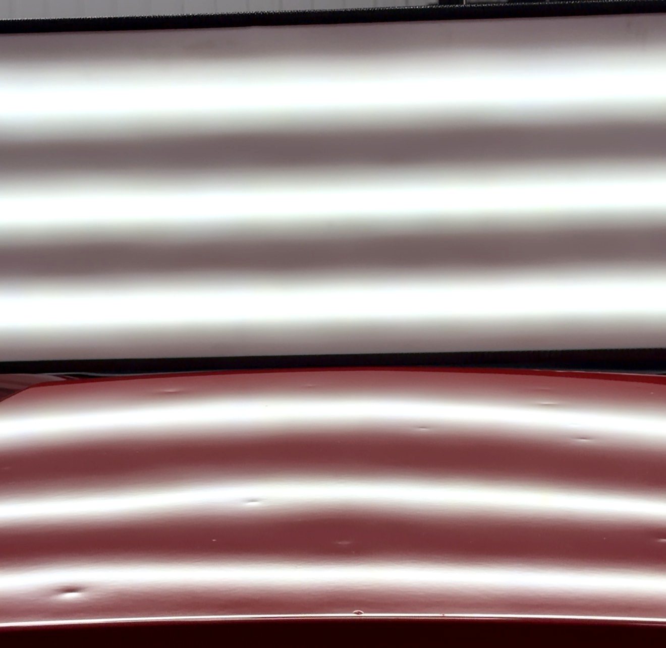Hail dents across a red vehicle panel shown under a PDR reading board
